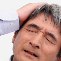頭痛で頭を押さえる中年男性
